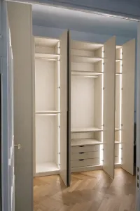 Interior accessories of the wardrobe shown in this picture:

- 35mm thick shelves made of melamine with a wood design in ivory color,
- triple drawers made of melamine with a wood design in ivory color,
- LED lights integrated into the wardrobe (vertical orientation),
- hanging rod in IVORY.

Corner wardrobe - Berlin, Germany - FB 211 Stony Ground lacquered matte with integrated handles. 

Our customer’s comment: The best wardrobe I’ve ever had! From the quality to the look, it’s an absolute 10/10! The custom color finish and the integrated lighting are especially worth mentioning. The delivery for our first wardrobe went perfectly. For our second wardrobe, it turned out to be a bit more difficult. However, IDAW has already addressed the issue and hired a new shipping company!

The exact measurements of the corner wardrobe are: left side width 169 cm, right side width 266.5 cm, height 294 cm, and depth 61 cm.