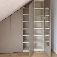 Interior accessories of the wardrobe shown in this picture:

- 35mm thick shelves made of melamine with a wood design in ivory color.

Sloping roof wardrobe: every roof has a different slope, so we offer our configurator, which adapts perfectly to your measurements to create a practical and functional wardrobe design customized to your needs. Everything is neatly enclosed behind personalized color doors. This wardrobe is installed in our customer’s house in Watt, Switzerland - FB 243 Charleston Gray matte lacquered with integrated handles.